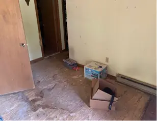 Bedroom after the clear-out with a bare subfloor and one box left by the door
